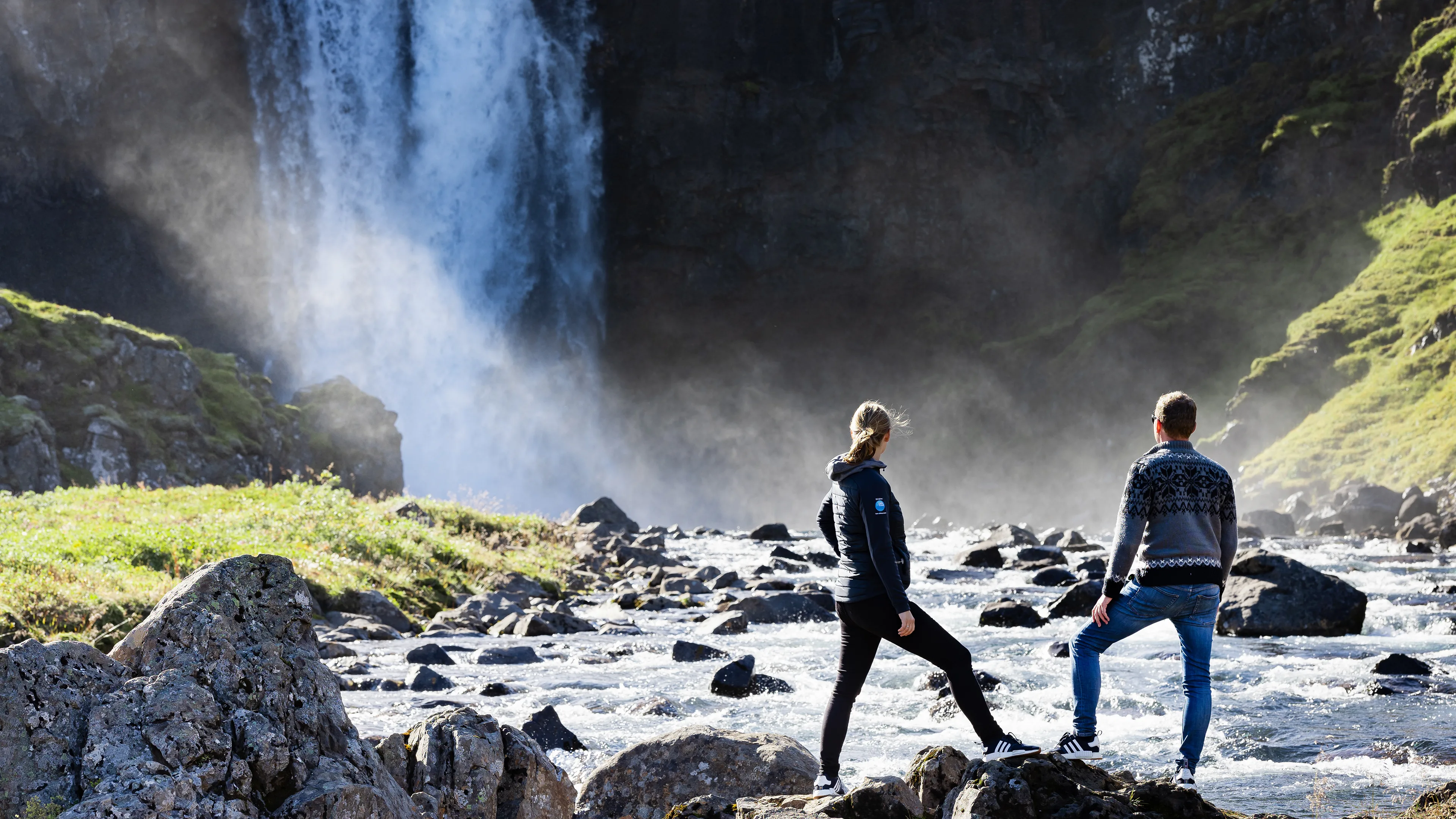 Paar am Wasserfall auf Island Paar am Wasserfall auf Island, Sprüh-Nebel durch herabstürzendes Wasser, Sonnenstrahlen, kleine Felsen im Wasser