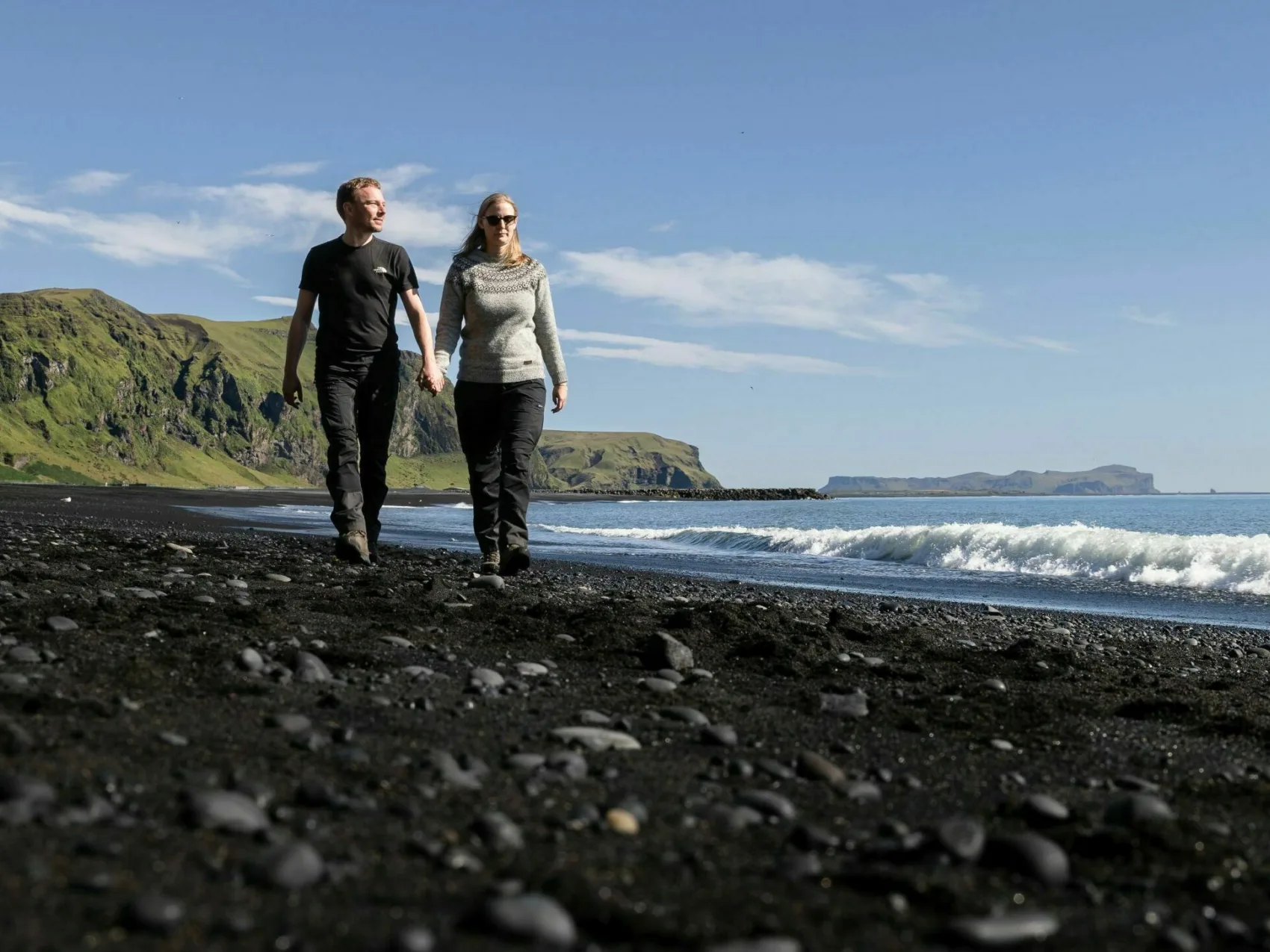 Island Strandspaziergang in Vík Island Strandspaziergang in Vík, Pärchen läuft Händehaltend am Strand entlang bei Sonnenschein