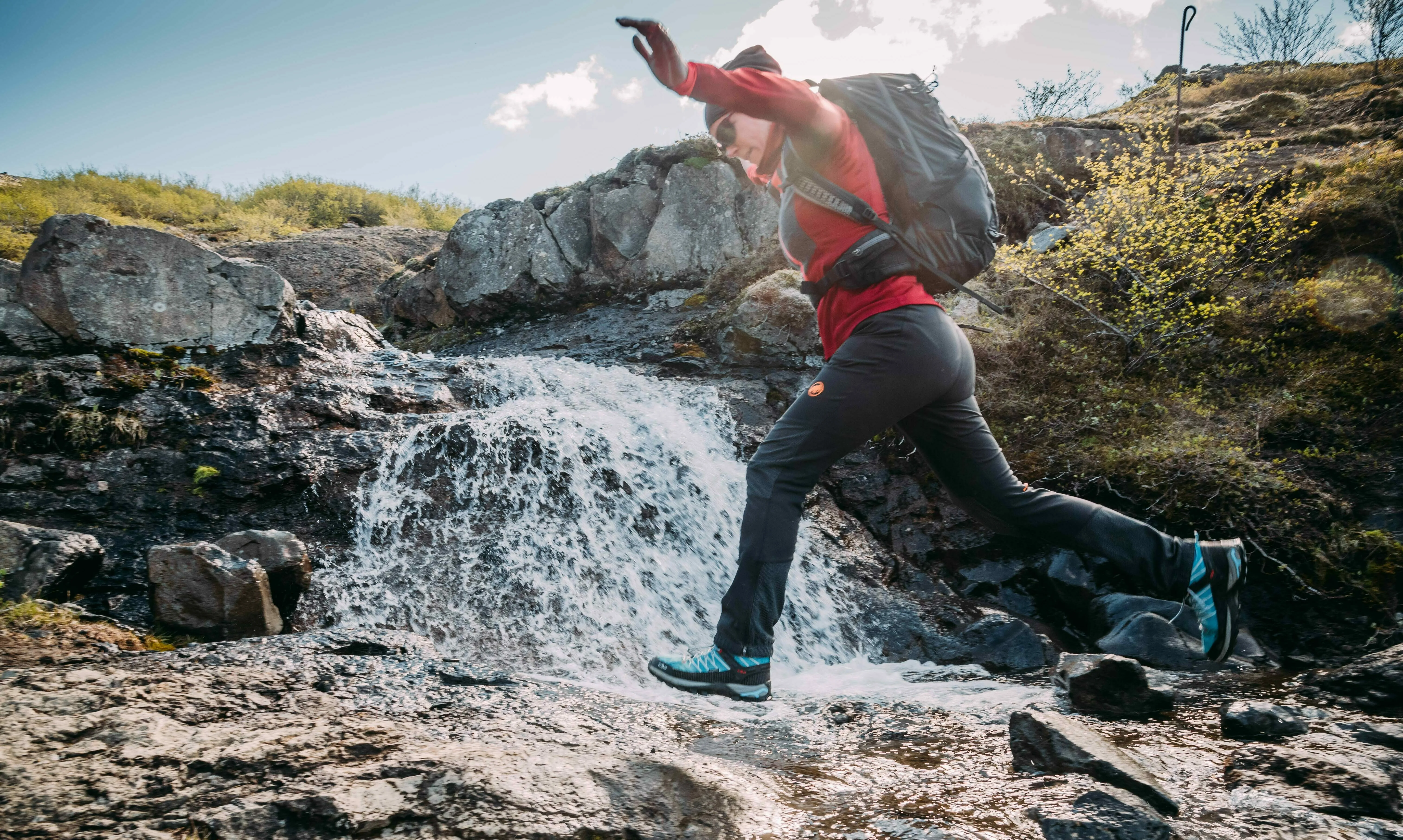 Unsere Kollegin springt über einen Bach in Island Mitarbeiterin von Katla Travel springt über einen Bach in Island